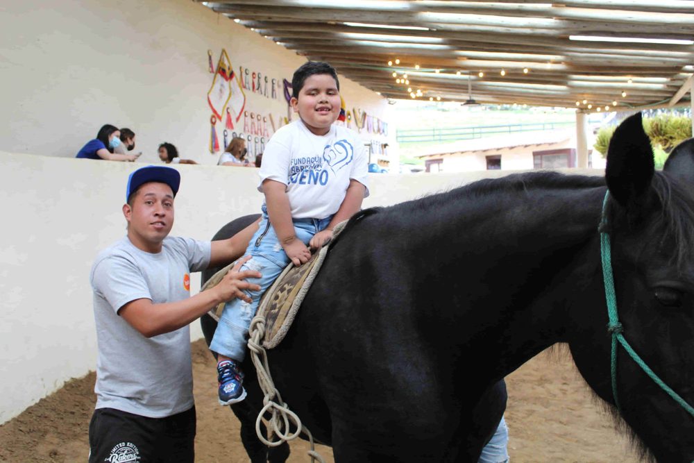Breynner sonríe montando a caballo, acompañado por un voluntario
