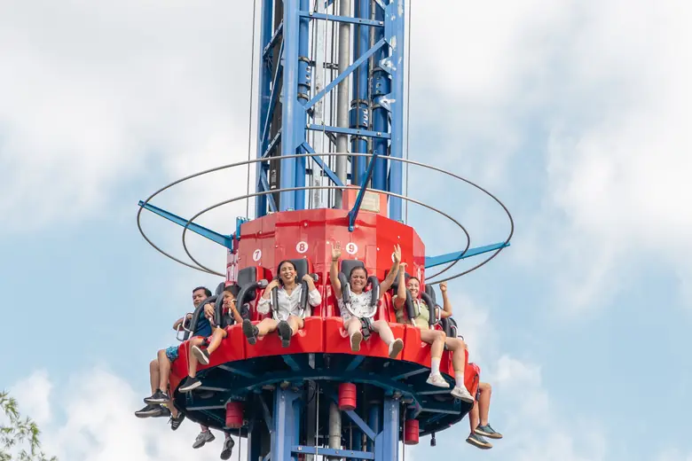 Niños y mamás levantan los brazos en lo alto de la torre de caída del Parque del Café