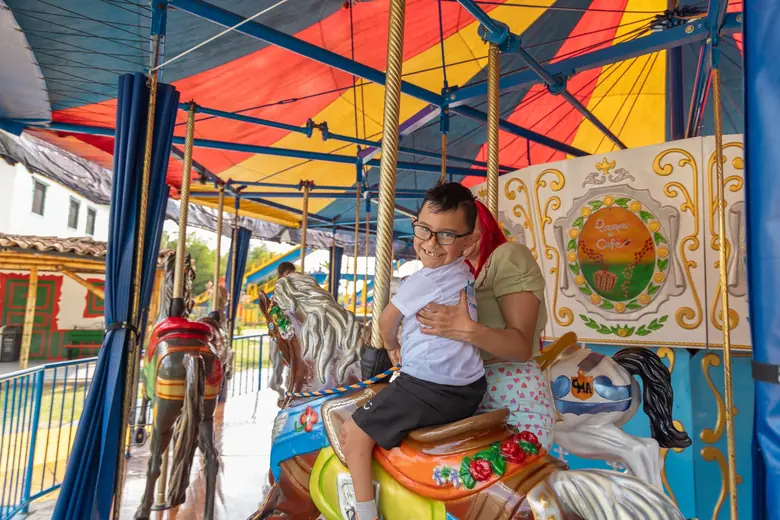 Un niño monta en el carrusel del Parque del Café junto a su mamá